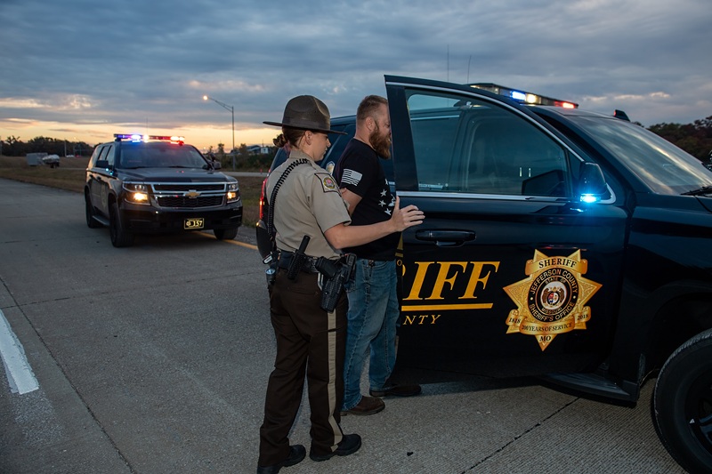 male officer placing subject in handcuffs into police vehicle.